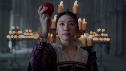 Jin Cheng (Jess Hong) holds up an apple while standing in front of an array of candles, in episode 103 of 3 Body Problem