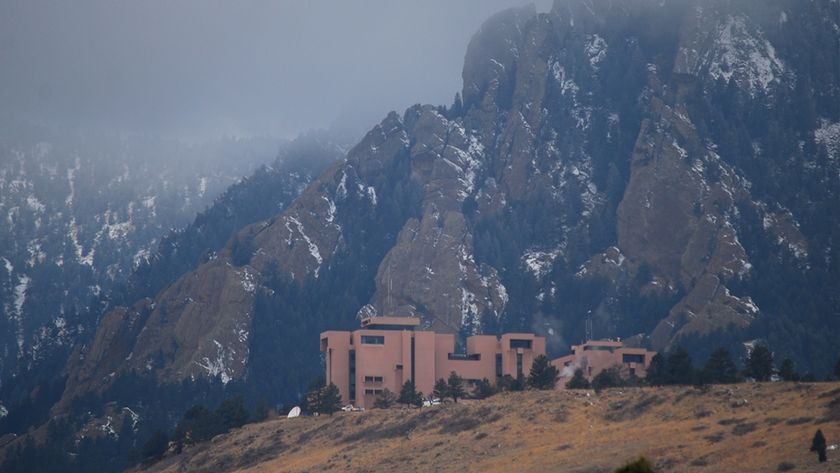 A series of adobe red buildings on a hillside with snowy mountains in the background
