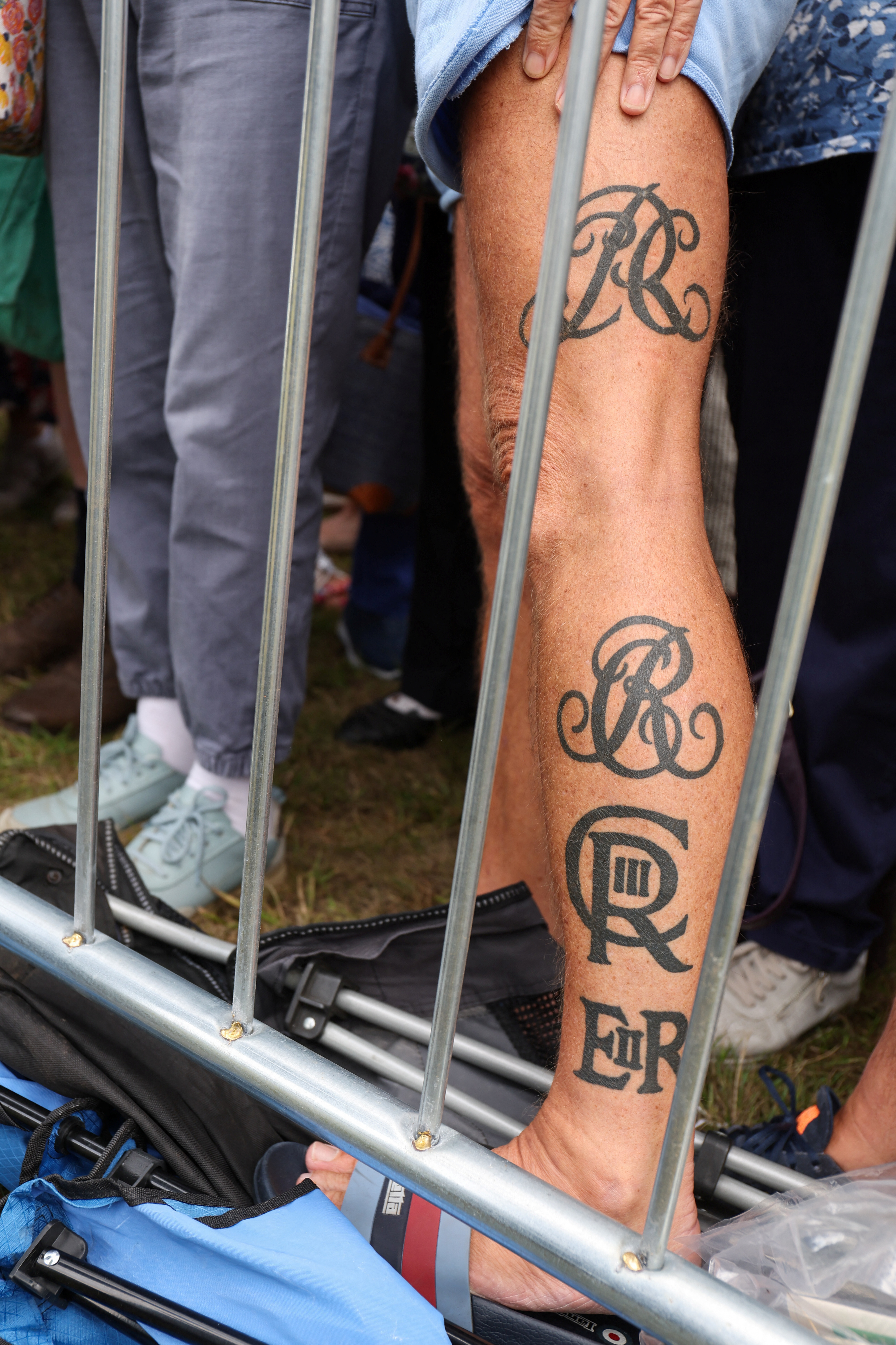 A man showing his leg covered in royal tattoos featuring Queen Camilla, King Charles and Queen Elizabeth's ciphers