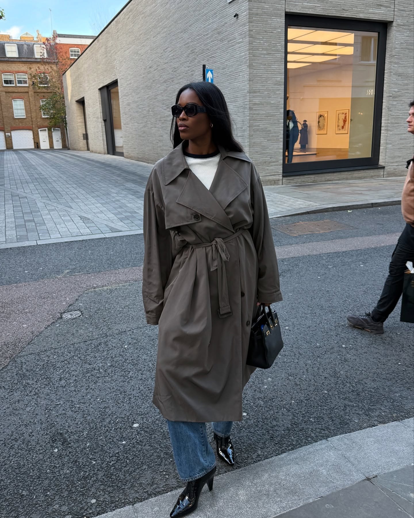Woman wears a trench coat, white ringer t-shirt, straight jeans and patent leather ankle boots.