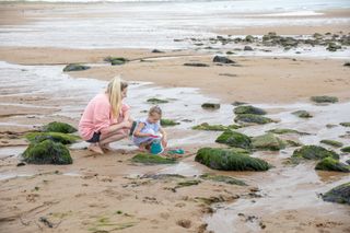 Mother and daughter looking in rock pools at the beach