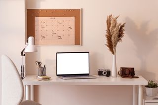 A desk set up with a laptop, stationery, a calendar, and an ornament with pampas grass.