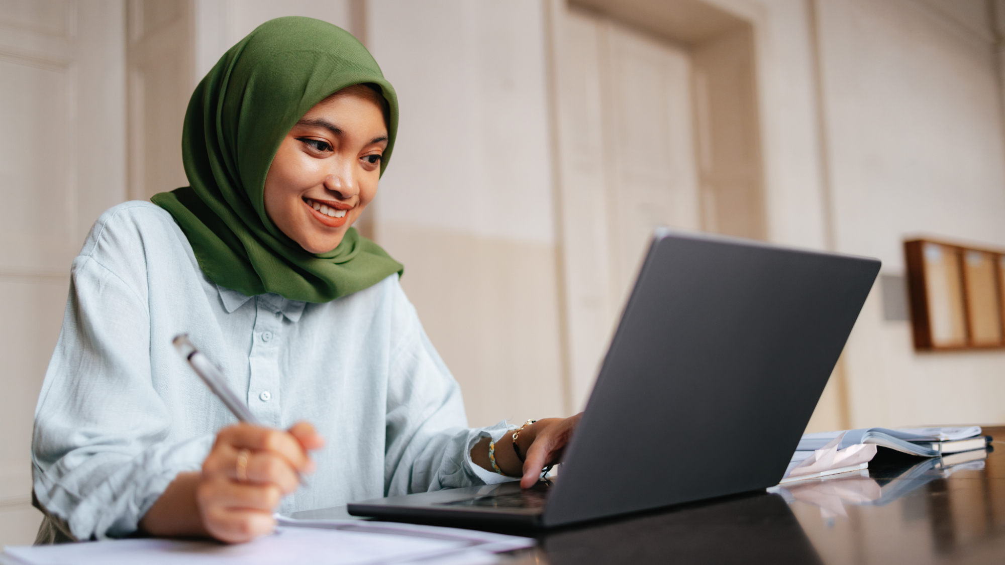 Indonesian student wearing hijab, sitting and using a laptop computer. 