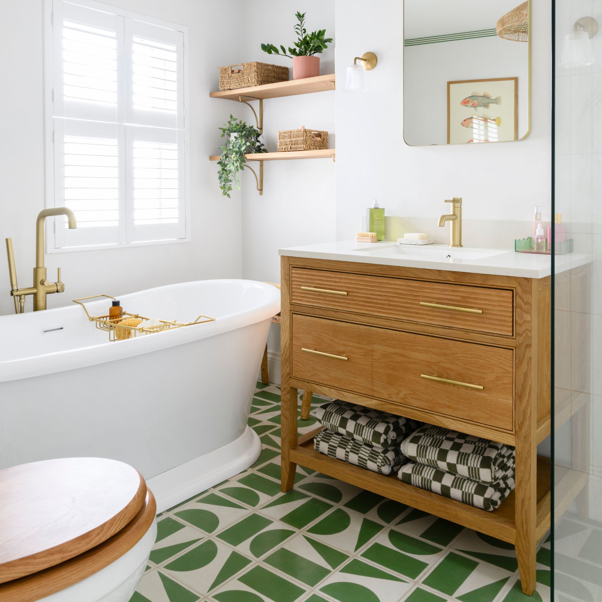 White painted bathroom with green and white floor tiles, a wooden sink vanity unit, and a freestanding white bath