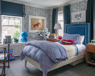A teenage boys bedroom idea with black and white zigzag wallpaper, a blue velvet headboard and blue blinds