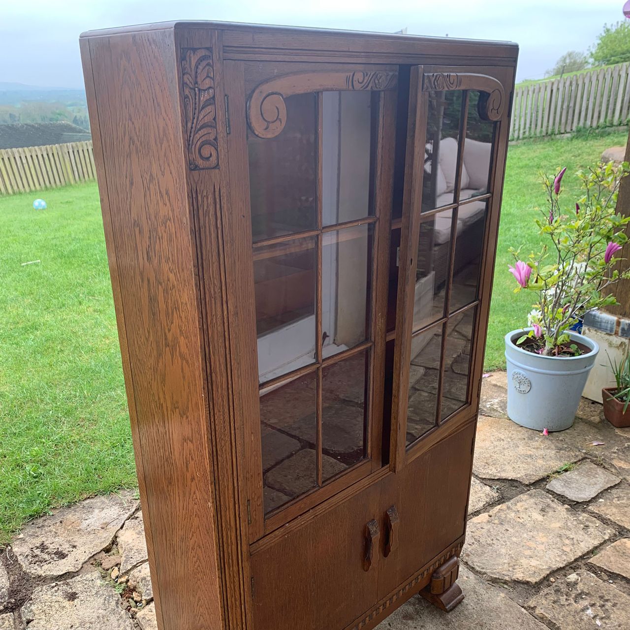 Empty wooden glass fronted cabinet on paved patio in garden