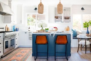 Kitchen color ideas in a white scheme with blue kitchen island, orange bar stools, rattan pendant lighting and wooden flooring.