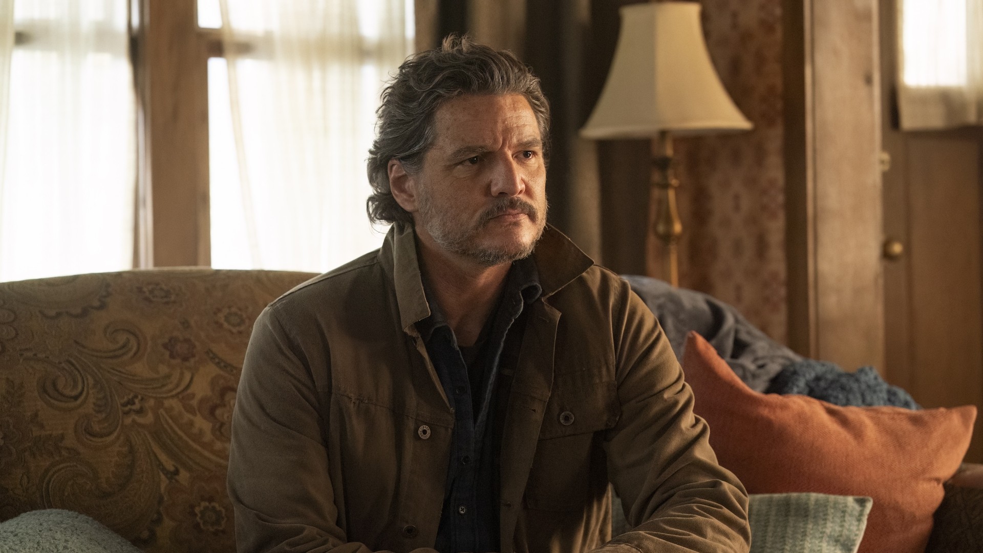 Pedro Pascal in The Last of Us sitting on a sofa in a living room.