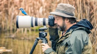 Wildlife photographer with kingfisher sitting on his telephoto lens