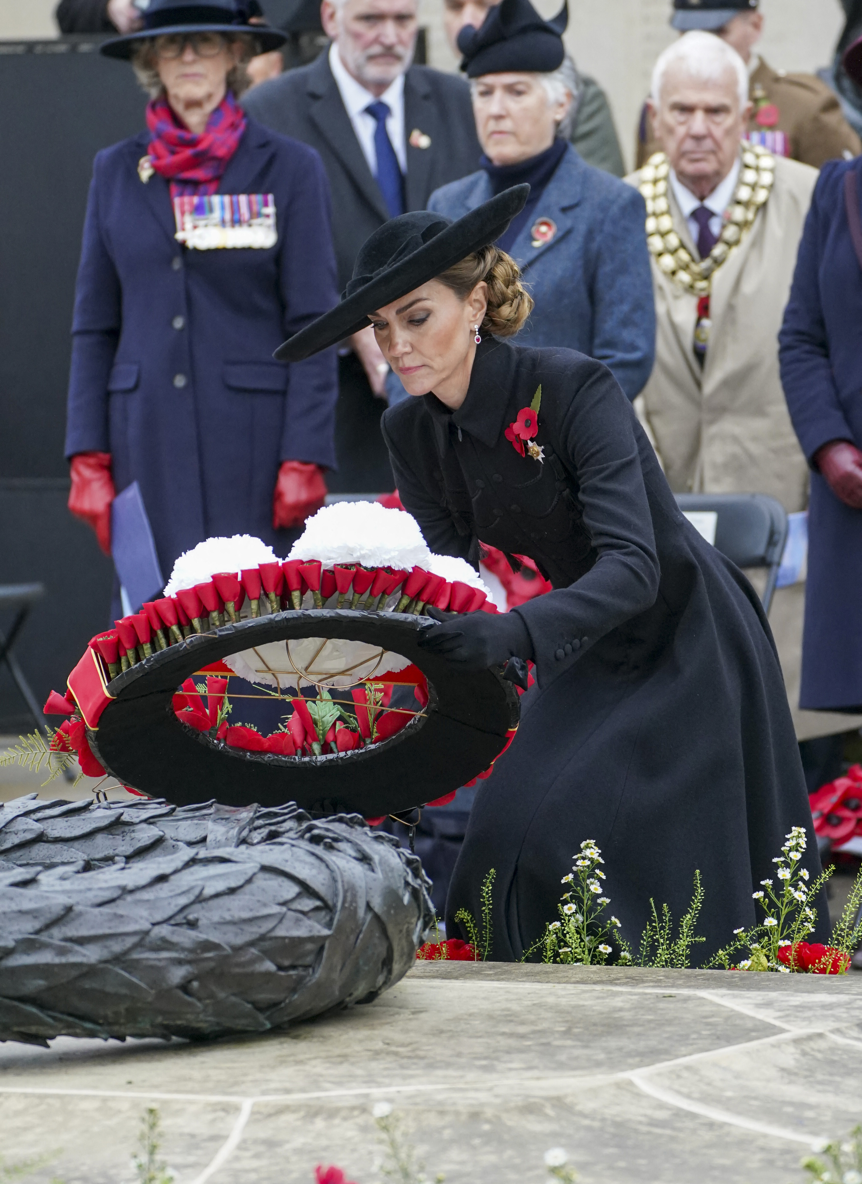 Kate Middleton wearing a black coat leaning down to lay a wreath