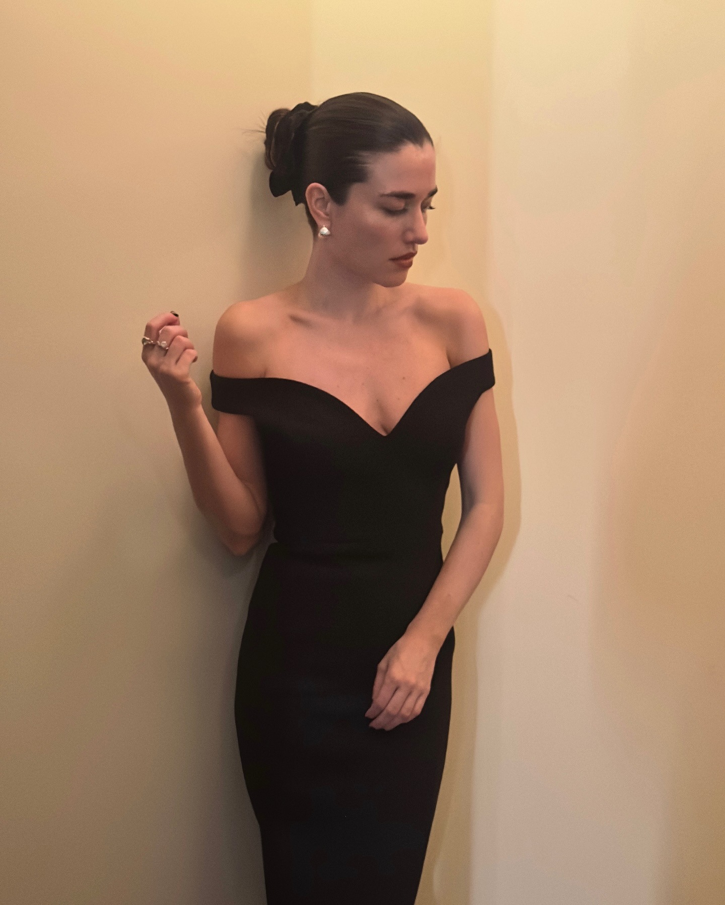 A woman wearing a black, off-the-shoulder velvet dress and slicked-back bun with a matching scrunchie.