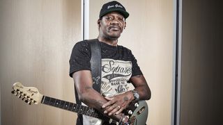 Eric Gales stands in a photo studio holding his signature Magneto RawDawg electric guitar