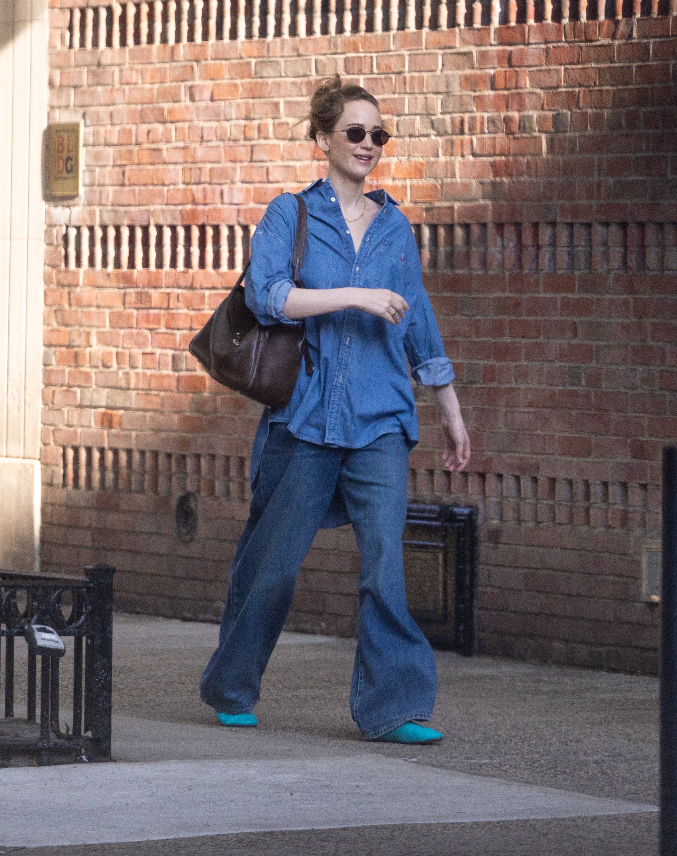 Jennifer Lawrence walks down the street in New York wearing baggy blue jeans with a denim skirt and bright blue shoes.