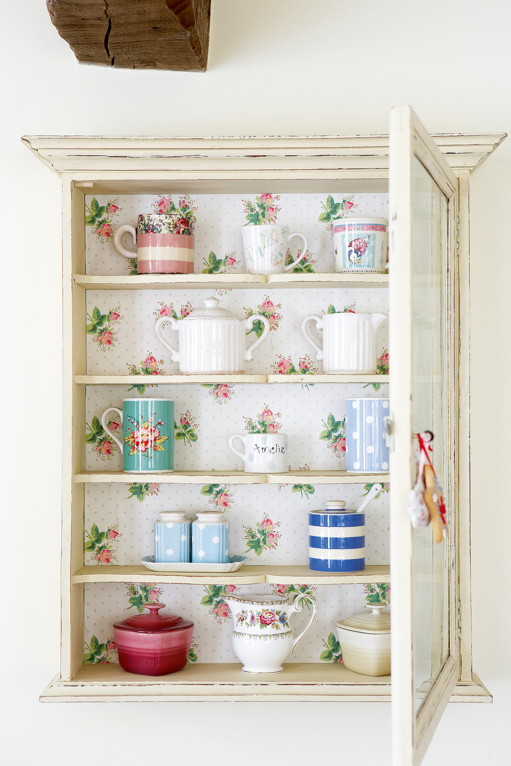 styling shelves: cupboard with pretty patterned wallpaper as backdrop styled with teacups