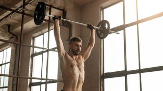 Man performing a barbell overhead press with the bar extended over his head in the gym