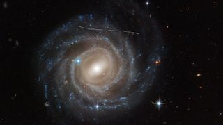 A spiral galaxy with a dashed line of light streaking across the image