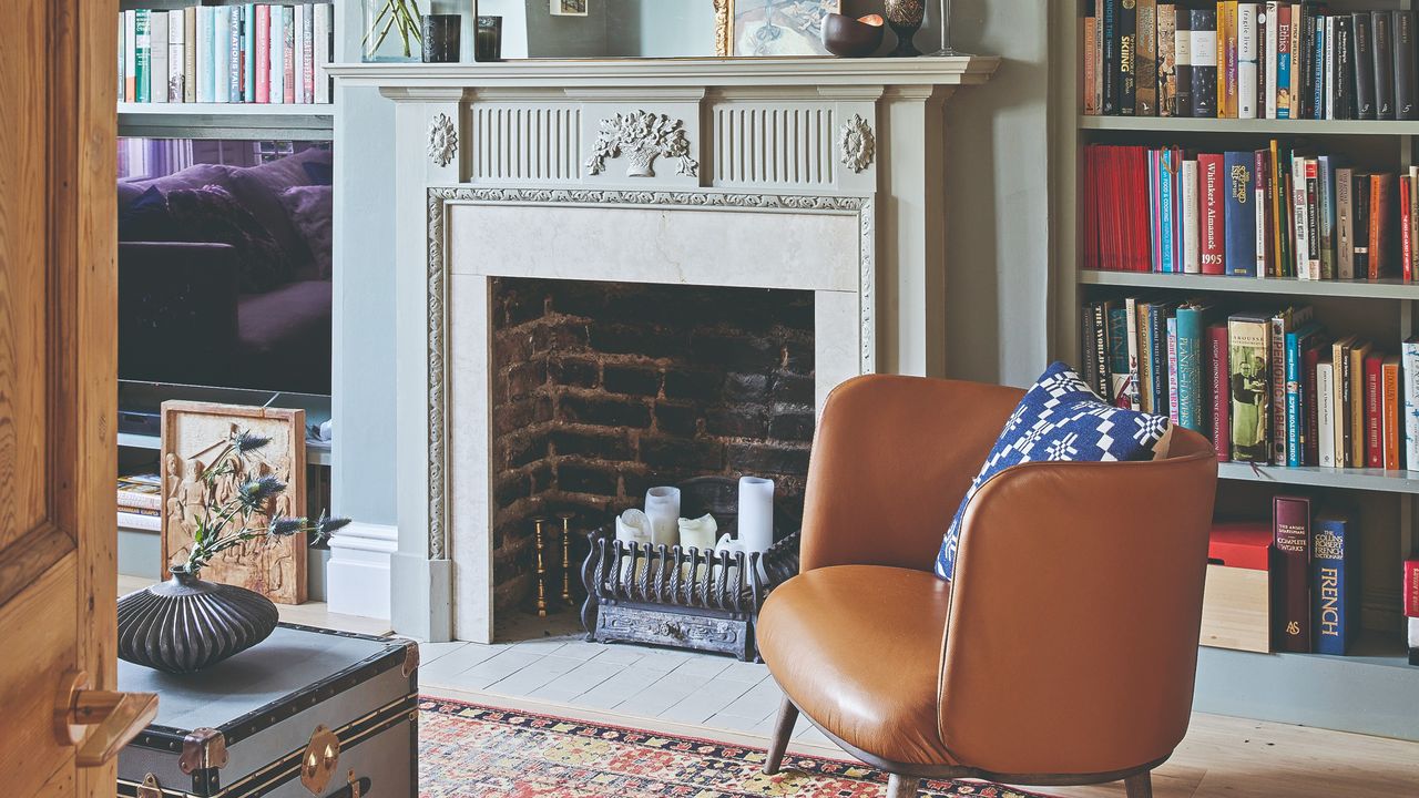 A living room with an ornate marble fireplace filled with candles and a brown leather chair set in front of it