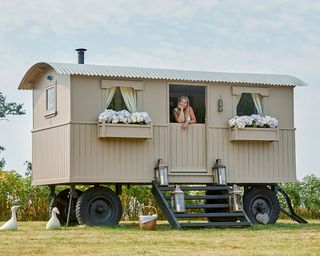 A shepherd's hut with floral window boxes and steps with lanterns on them leading up to a stable door