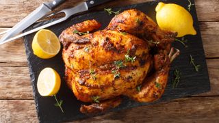 A roast chicken next to lemons and a carving knife