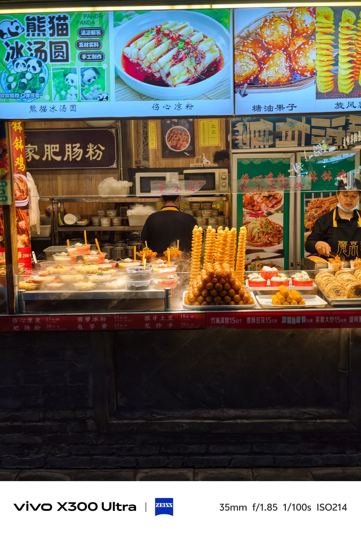 A brightly lit Chinese street food stall showcasing pyramids of snacks and bowls of local dishes.