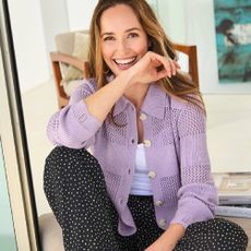 A happy women wearing a purple cardigan and black and white spotty trousers from Cotton Traders.