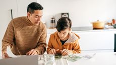 A father and son sit at a kitchen island and work with cash and a calculator.