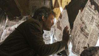 Joel (Pedro Pascal) peers through a window covered in newspaper in The Last Of Us episode 4