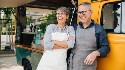 Happy mature couple looking away while standing against food truck