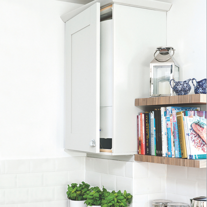 A hot water boiler stored in a tall wall kitchen cupboard unit, with shelves and wood worktop.