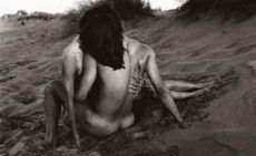 black and white photo of a pair of nude bodies kissing and sitting on a sandy beach