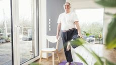 Man stands on one leg holding on to a chair