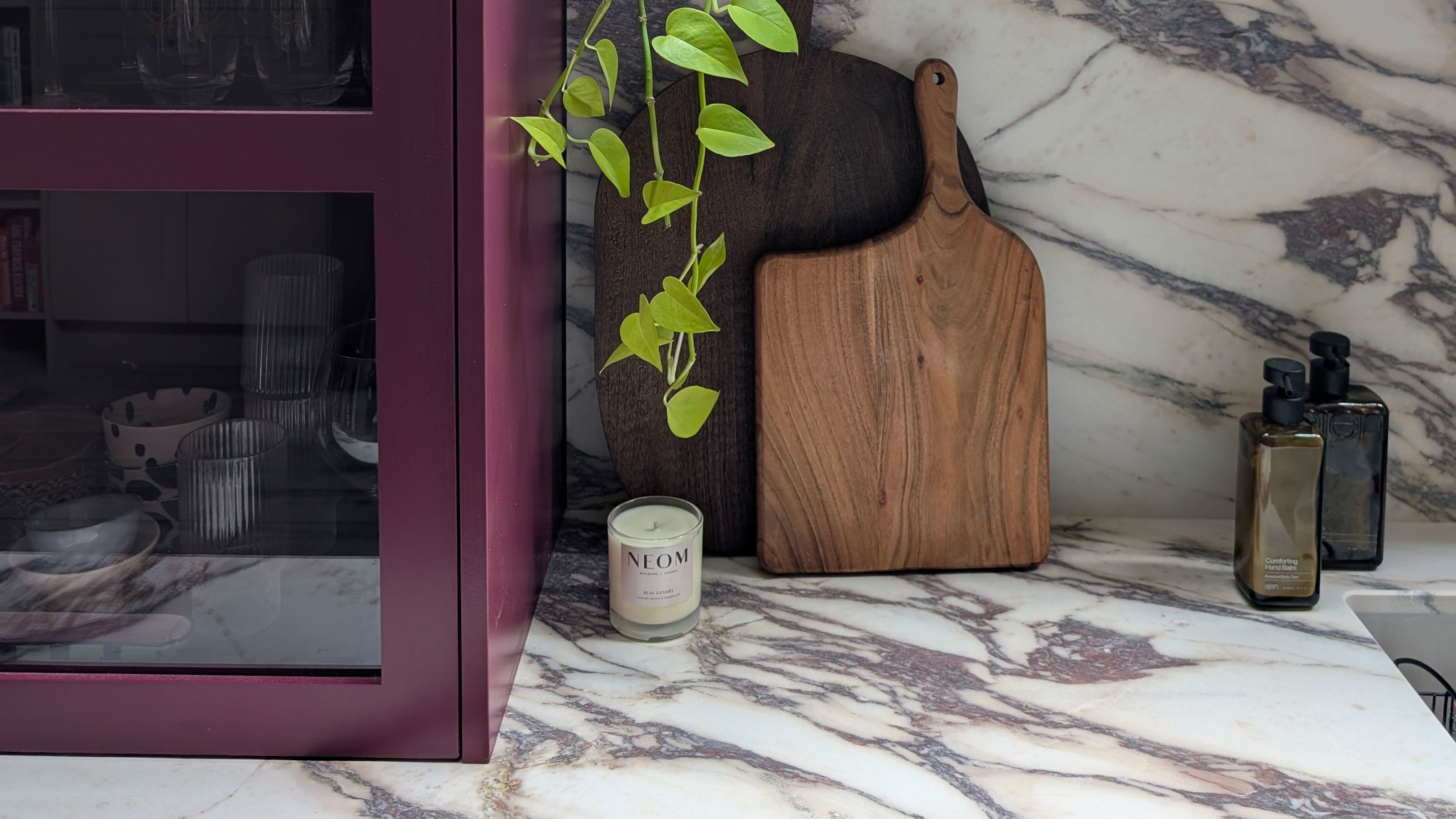 Close up of marble style worktop and splashback with berry-red cabinet and wooden boards
