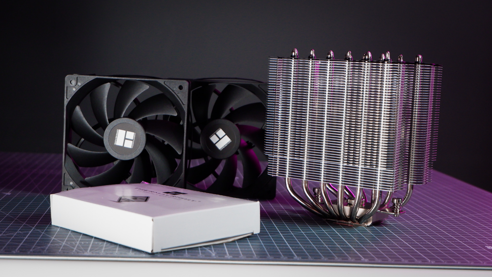 A Thermalright Peerless Assassin 120 SE cooler on a desk with the fans beside it.