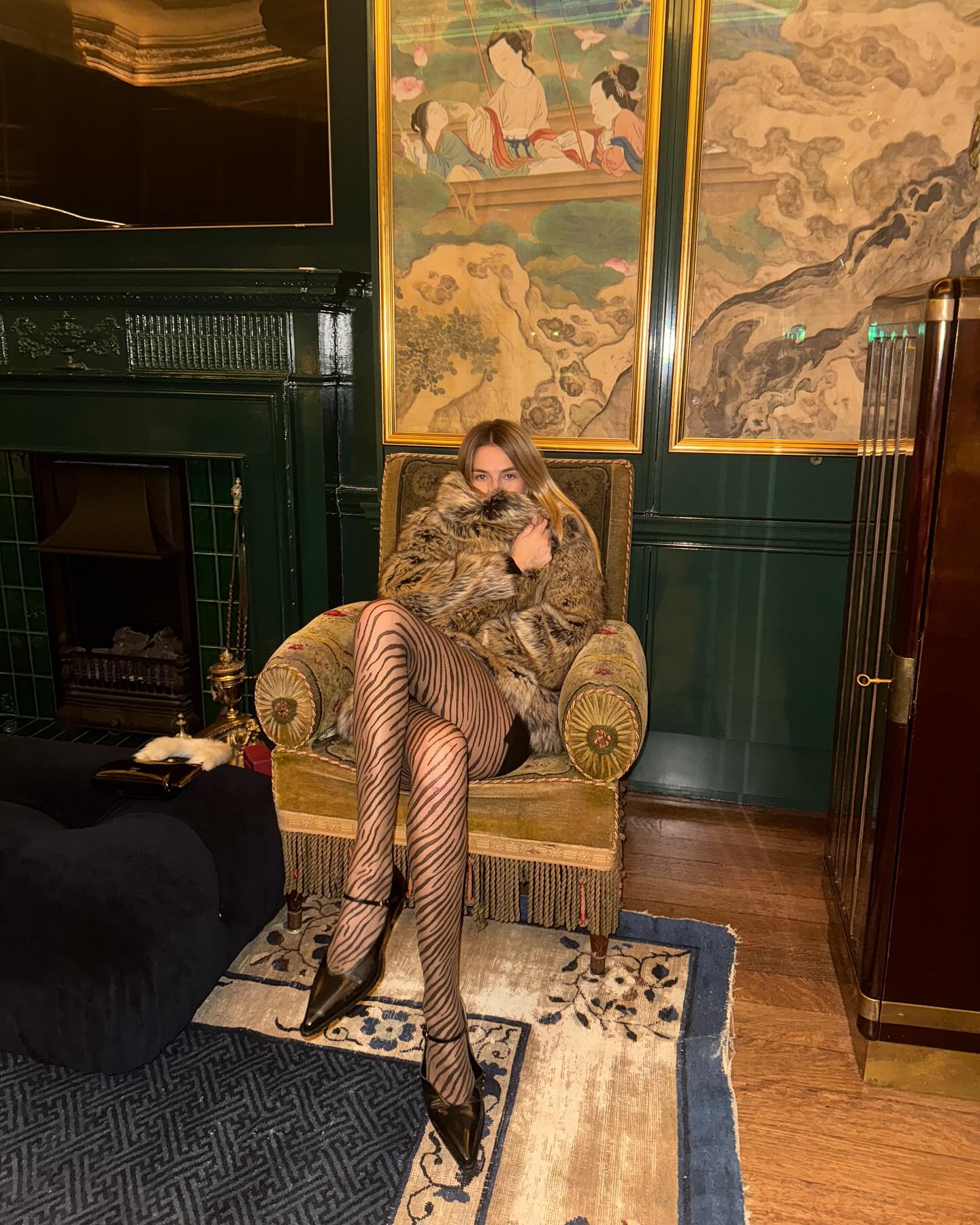 An image of @camillecharriere wearing tiger-print tights from Swedish stockings with a fur jacket and black pointed toe heels.