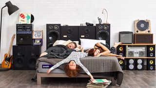 A couple and their young daughter relax on the Purple Mattress in a bedroom filled with music equipment