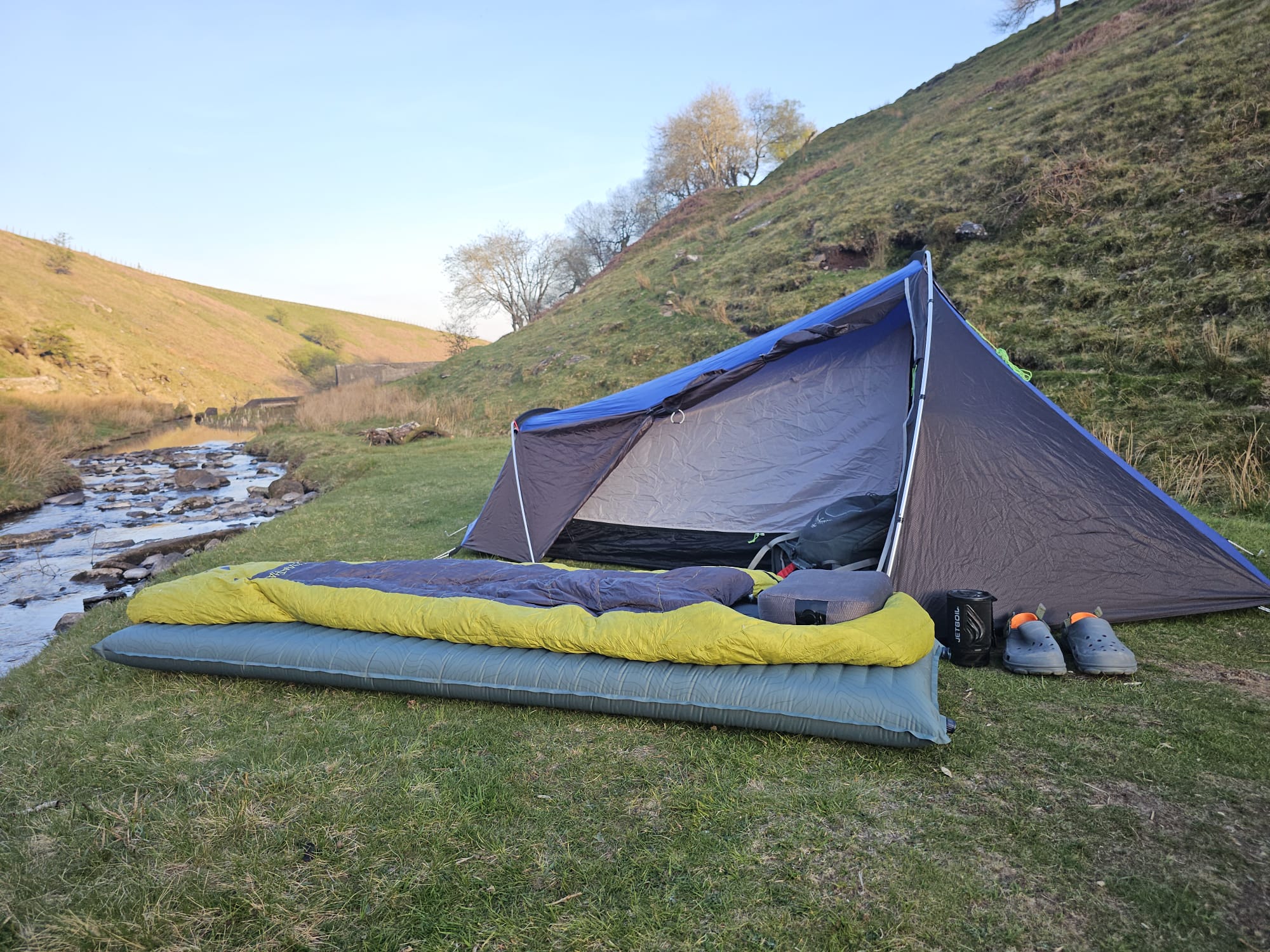 A sleeping pad and sleeping bag in front of a small backpacking tent