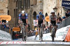 Three men cycle over a finish line