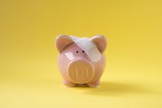 Piggy bank with plaster on forehead on yellow background.