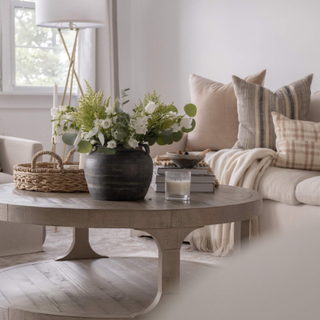 Neutral lounge detail with round washed-wood coffee table, styled with coffee table books and fresh flowers in vase, and comfy sofa with tactile scatter cushions.