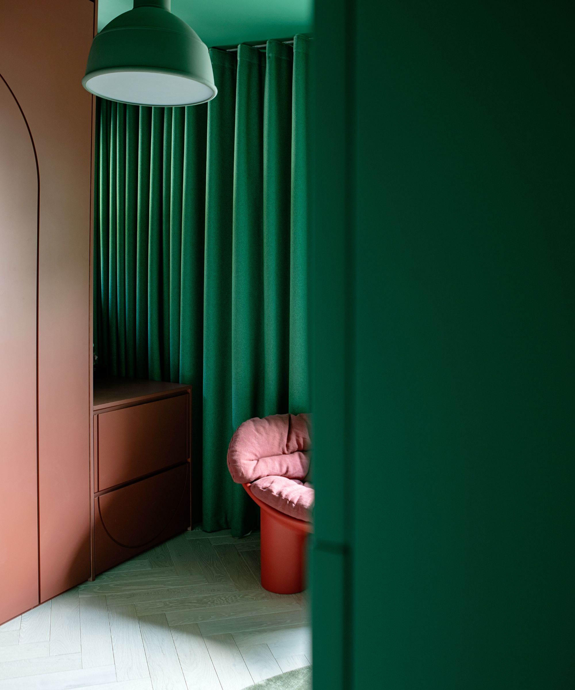 a living room with bold green walls and curtains, contrasted to an oxblood red built in cabinet and red chair