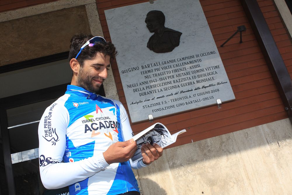 Aviv Yechezkel reads a book on Bartali in front of a plaque at the Terontola train station