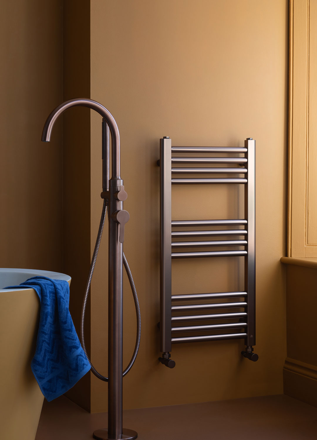 brushed chrome heated towel warmer in yellow bathroom with floor mounted tap