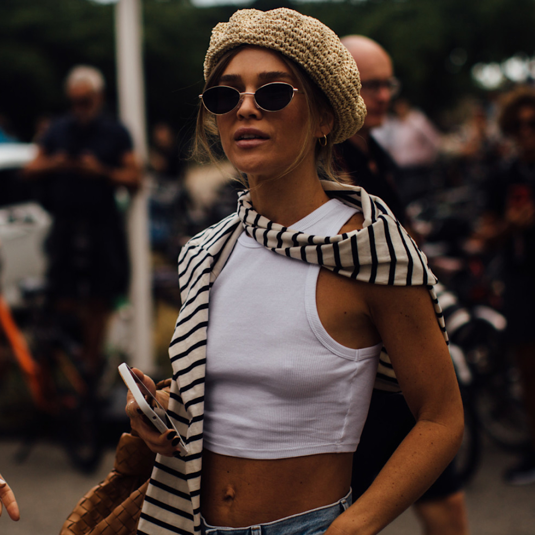 woman in copenhagen spring 2023 fashion week wearing white tank top striped shirt over her shoulder sunglasses and beanie hat 