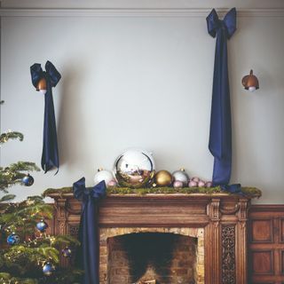 An antique fireplace decorated with large blue bows and metallic Christmas baubles