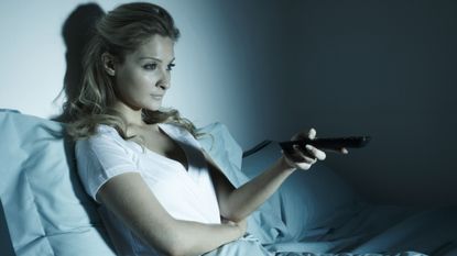Woman sitting up in bed pointing a TV remote