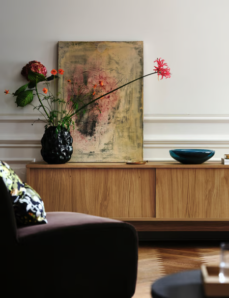 Warm neutral living room featuring a wooden sideboard, velvet accent chair, and irregularly textured vase