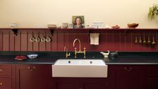 A burgundy and beige kitchen with black countertops and a paneled kitchen backsplash