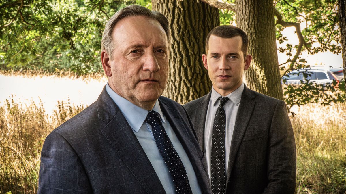 Neil Dudgeon and Nick Hendrik in suits as DCI John Barnaby and DS Jamie Winter stand in front of a tree in Midsomer Murders