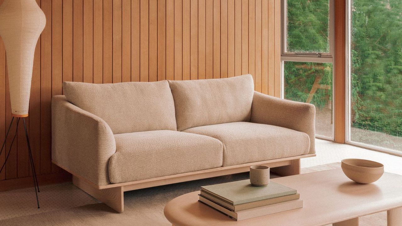 A minimalist living room with a cream couch and a wood panelled wall