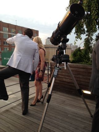 Two party-goers look out onto the Manhattan skyline next to a telescope pointed toward the star system Gliese 526. Image released June 18, 2013.